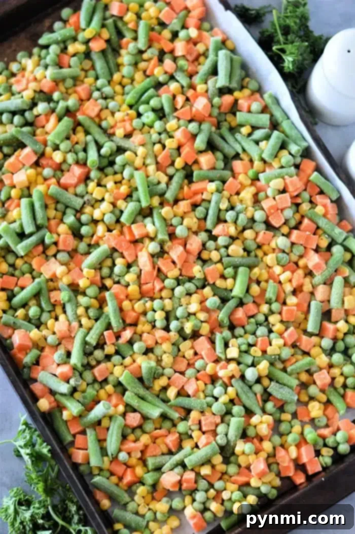 Frozen to Fantastic: Roasting Your Veggies 5 A spacious baking sheet laden with a colorful assortment of roasting frozen vegetables, including vibrant green beans, golden corn, tender peas, and uniformly diced carrots. The vegetables show signs of caramelization, with a sprig of fresh parsley peeking into the frame from the background, adding a touch of freshness.