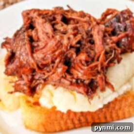 A savory Beef Manhattan graces the table, featuring a slice of toasted bread topped with creamy mashed potatoes and shredded beef, all elegantly presented on a white plate with a woven placemat underneath.