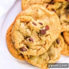 A delightful pile of dairy-free chocolate chip cookies sits on a white plate, tempting with its rich aroma and chewy texture.