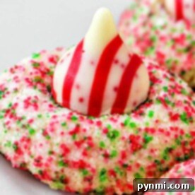 Blooming Bites 6 A close-up of a Hershey Kiss Christmas cookie topped with a striped chocolate, coated in red and green sugar sprinkles for a festive touch.