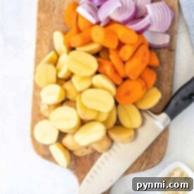 Chopped potatoes, carrots, and red onions on a wooden cutting board await a knife's touch; spices in small bowls nearby enhance the flavor of steaming vegetables in a microwave.