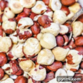 A close-up of a bowl brimming with shelled and unshelled hazelnuts, accompanied by a metal spoon hinting at the next step: learning how to roast hazelnuts for that perfect toasty flavor.