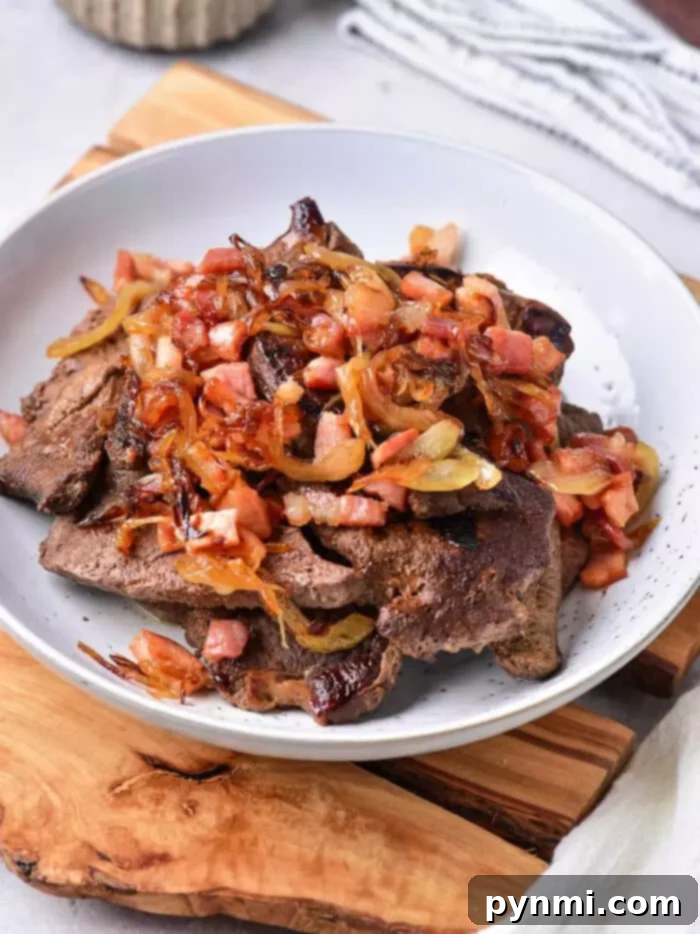 Tender Pan-Fried Beef Liver with Caramelized Onions 2 A white bowl filled with cooked liver pieces topped with sautéed onions and diced bacon bits, showcasing a delicious beef liver recipe.