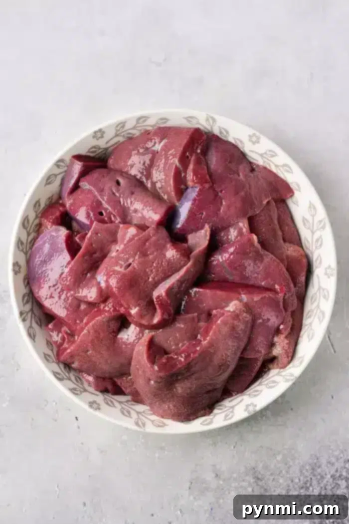 Tender Pan-Fried Beef Liver with Caramelized Onions 3 A white bowl filled with raw, sliced chicken liver sits on a light gray countertop, ready for preparation.