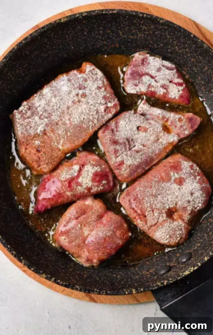 Tender Pan-Fried Beef Liver with Caramelized Onions 5 A frying pan with six pieces of liver being cooked in oil. The liver pieces appear to be seasoned with a coating of flour, illustrating how to cook beef liver perfectly.