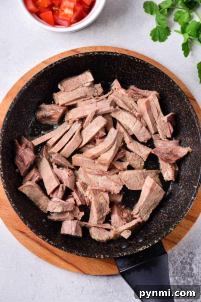 Sliced cooked tongue in a frying pan on a wooden board, next to cut tomatoes and cilantro. For those interested in expanding their culinary skills, learning how to cook cow tongue can offer a rich and delectable addition to your kitchen repertoire.