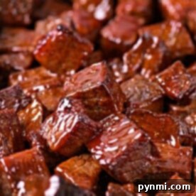 A tray filled with glazed, cubed pieces of barbecue chuck roast burnt ends, all glistening with sauce.