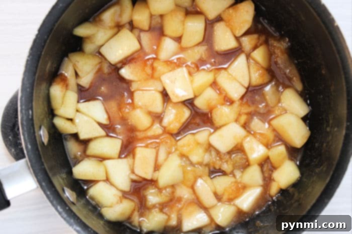 A bowl filled with a rich, spiced homemade apple pie filling, featuring tender apple chunks and a thick, glossy sauce, ready to be used in desserts.