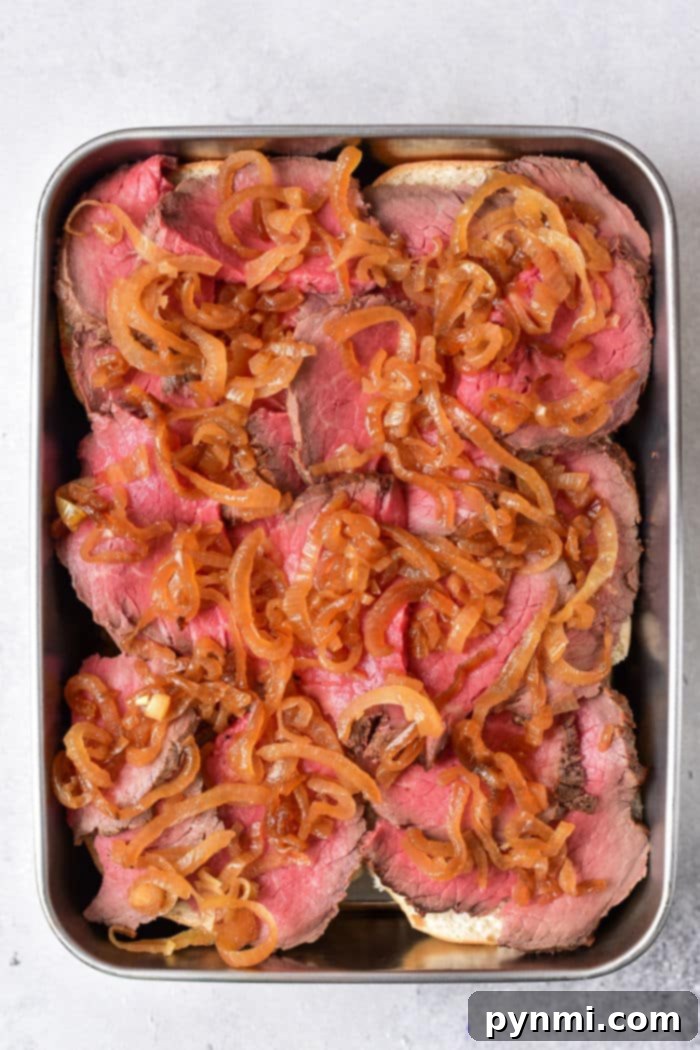 Close-up of an open-faced roast beef sandwich with melted cheese and caramelized onions.