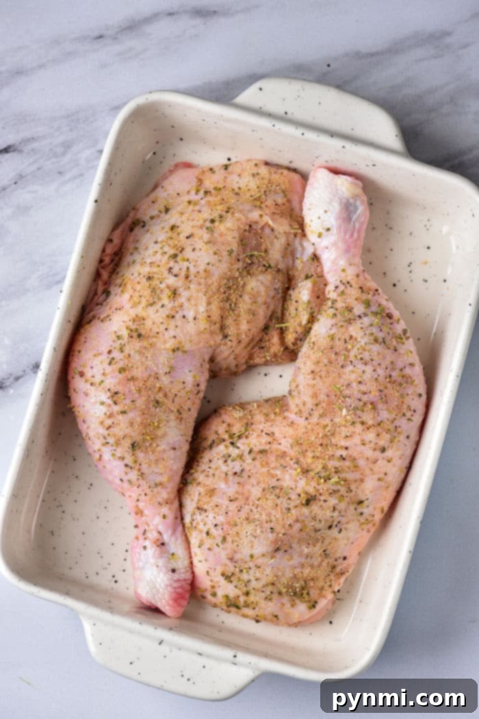 Raw chicken leg quarters seasoned and ready for baking in a glass dish.