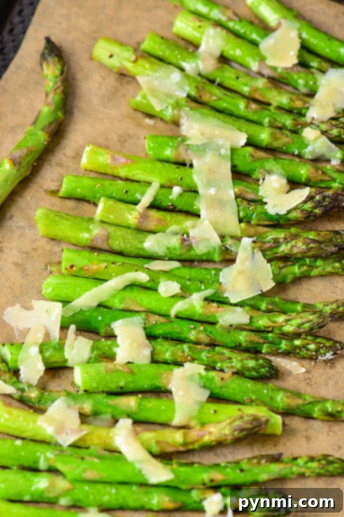 Baked asparagus topped with Parmesan cheese on a brown surface, offering the perfect guide on how long to cook asparagus in the oven for that tender, crisp bite.