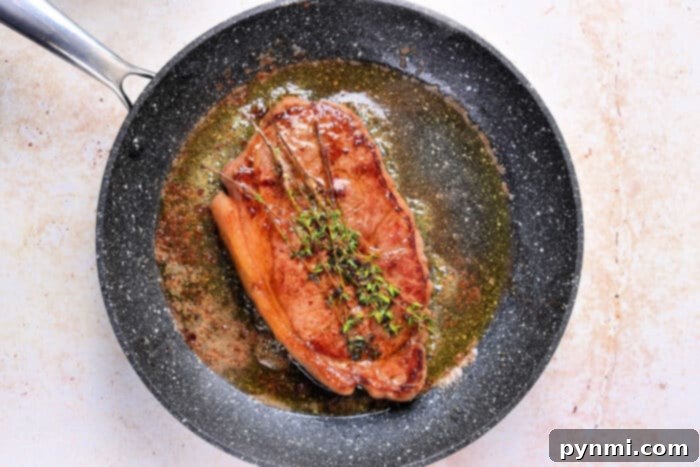 From Freezer to Flavor Sous Vide Steak 5 A perfectly cooked Sous Vide Frozen Steak with herbs and sauce in a black frying pan on a light surface.