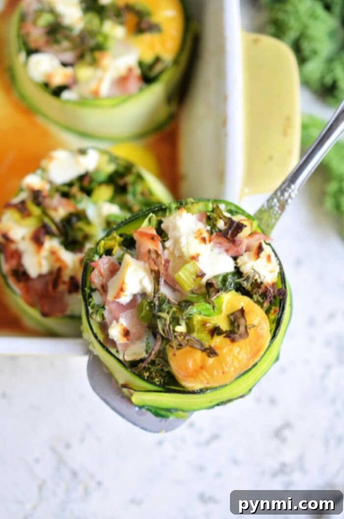 Sunny Zucchini Nests 2 Close-up of stuffed zucchini cups in a baking dish, filled with eggs, vibrant greens, savory ham, and melted cheese. One zucchini cup is being lifted with a silver spatula, showcasing the perfectly cooked egg and colorful ingredients. More zucchini egg nests are visible in the background.