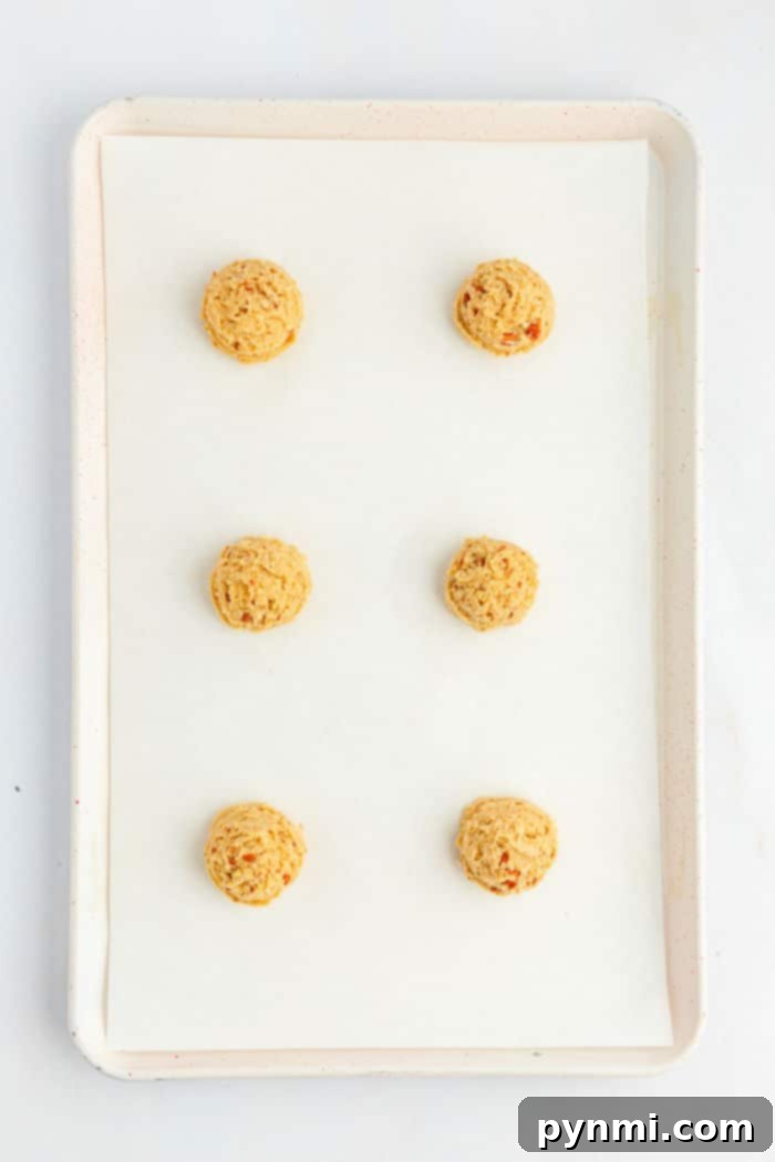 Buttery Pecan Cookie Bliss 3 A white baking tray lined with parchment paper holds six evenly spaced raw Bear Paw Cookies dough balls arranged in two columns and three rows. The tray is shown from above against a white background.