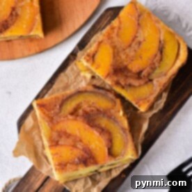 Two slices of delicious peaches cake rest on a wooden board with parchment paper, waiting to be savored, next to a gleaming fork.