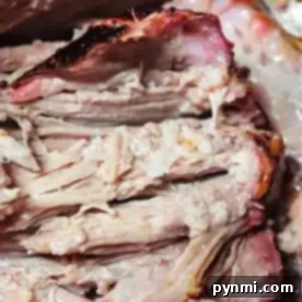 Close-up of sliced smoked pork roast showcasing tender, juicy meat and a reddish-brown crust. The texture appears soft and well-cooked, with visible layers and some charred edges. A fork is partially visible in the background.