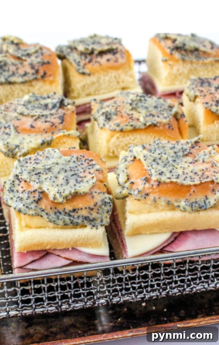 Air Fryer Sandwich Creations 7 Close-up of ham and cheese sliders on a wire rack, topped with a poppy seed and butter mixture. These air fryer sandwiches boast a layer of melted cheese, perfectly arranged in a grid pattern. The buns are lightly toasted to perfection.