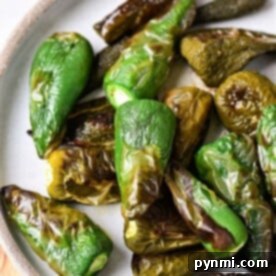 Smoky Oven Roasted Jalapenos 7 Roasted jalapeno peppers in oven, vibrant and smoky, rest elegantly on a ceramic plate.