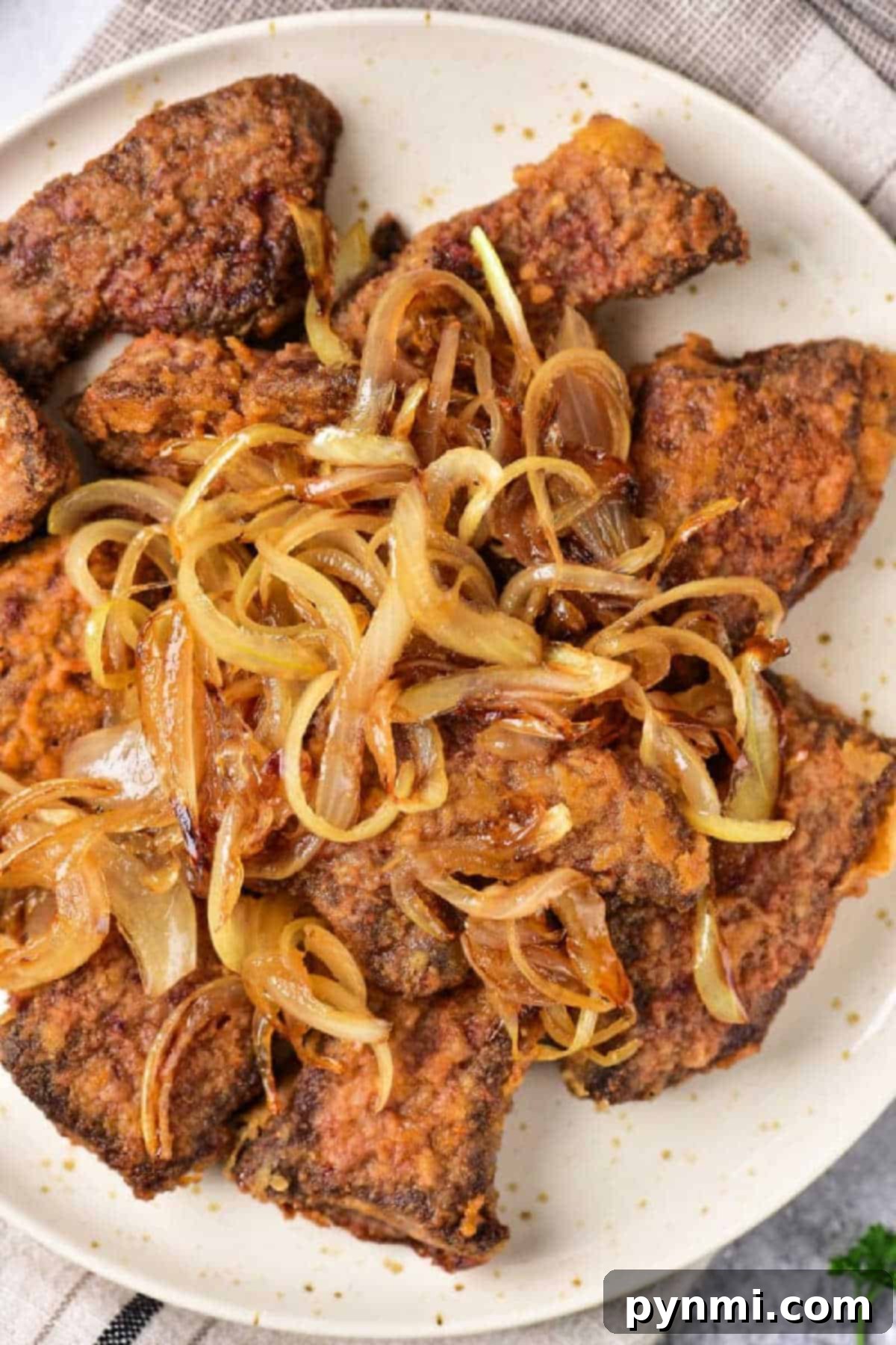Mastering Beef Heart: Tender Recipes and Techniques 2 Fried beef heart pieces topped with caramelized onions on a white plate—a classic dish for those learning organ meats, just like when discovering how to cook beef heart.