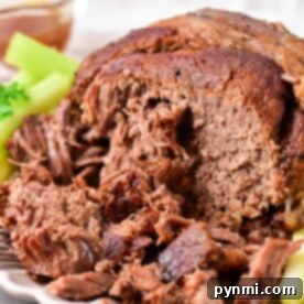 Close-up of tender beef roast shoulder shredded on a plate, adorned with a crisp garnish of celery and parsley.