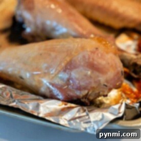 Close-up of a baked turkey leg resting on a piece of aluminum foil on a baking tray. The golden-brown exterior showcases the perfectly roasted appeal of baked turkey legs.
