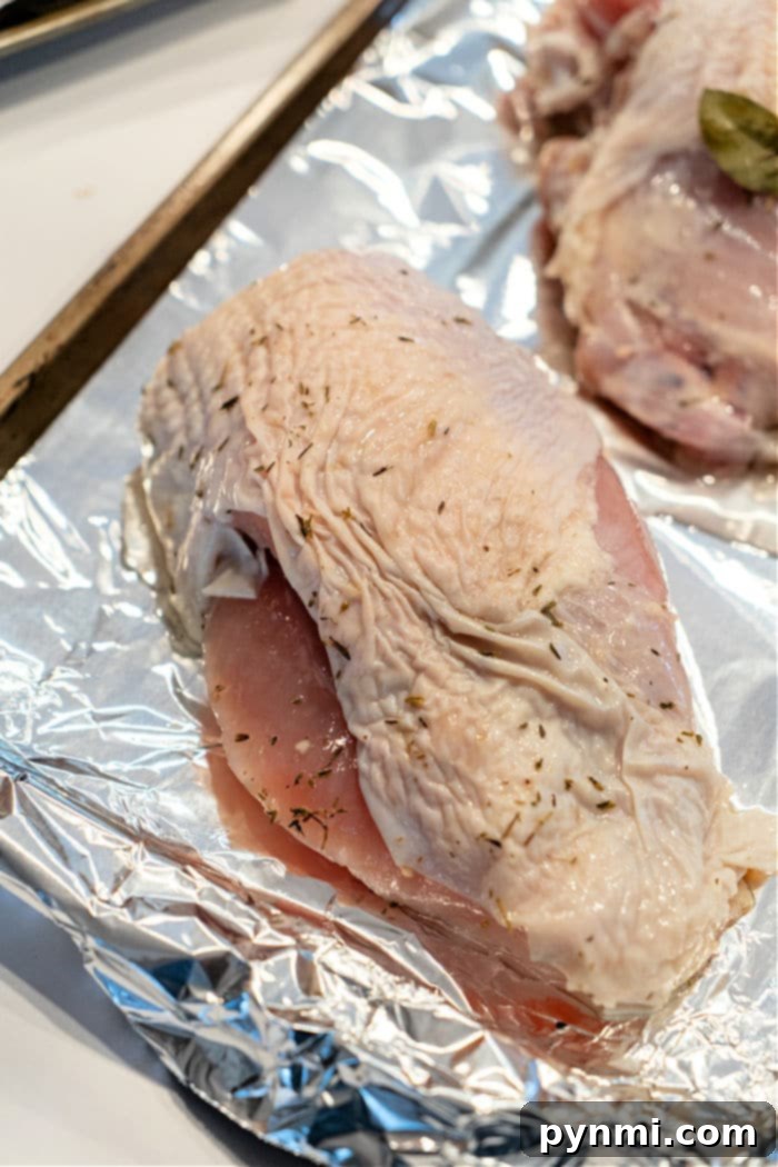 Raw turkey breast pieces, liberally seasoned with a blend of herbs and spices, are arranged on a foil-lined baking sheet, prepared for roasting. The textured surface of the skin and visible seasoning promises a rich, flavorful result. This setup demonstrates an essential step in "How to Cook a Butterball Turkey Breast," ensuring consistent tenderness and deliciousness with every preparation.