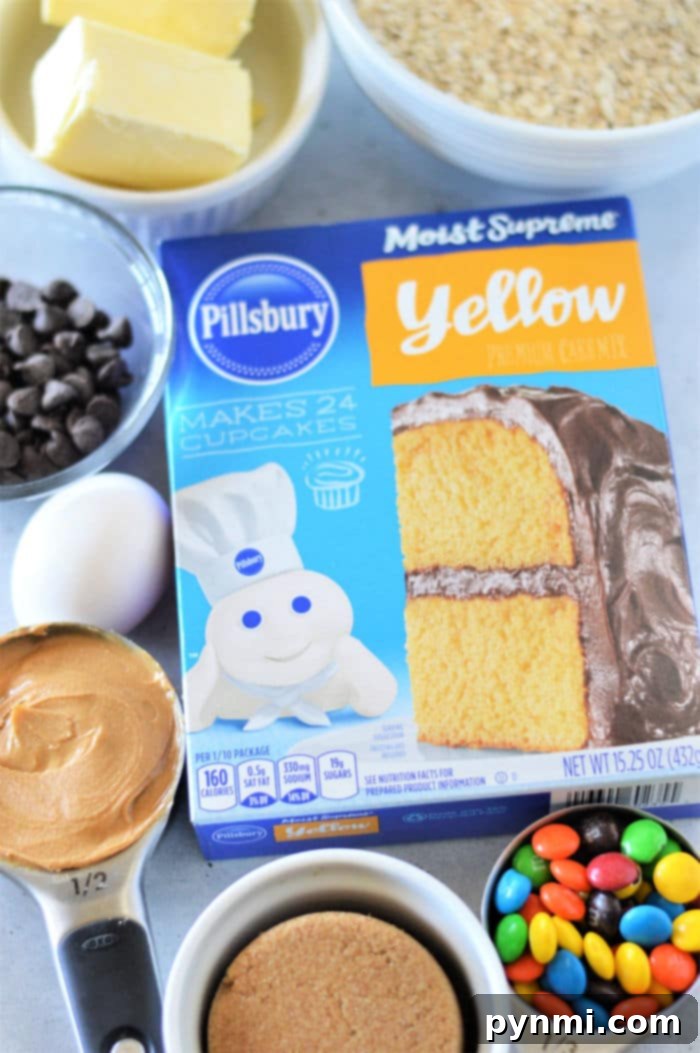 Effortless Cake Mix Cookie Bars 3 A box of Pillsbury Moist Supreme Yellow Premium Cake Mix surrounded by various baking ingredients, including a measuring cup with peanut butter, a measuring cup with brown sugar, assorted colorful candies, chocolate chips, an egg, and a stick of butter—perfect for making Cookie Bars From Cake Mix.