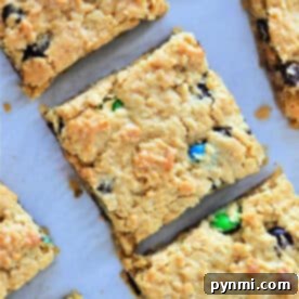 Golden cookie bars from cake mix studded with chocolate chips and colorful candy pieces, cut into squares on parchment paper.