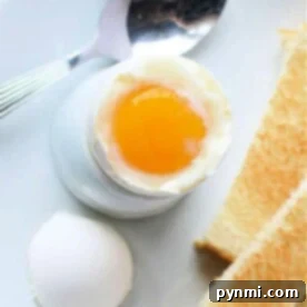 Air fryer soft-boiled egg in an egg cup, accompanied by toast slices and a spoon, all elegantly arranged on a white plate.