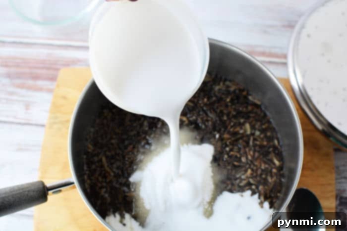 Pouring creamy coconut milk into a pot filled with black rice and sugar on a wooden surface, creating a luscious black rice pudding.