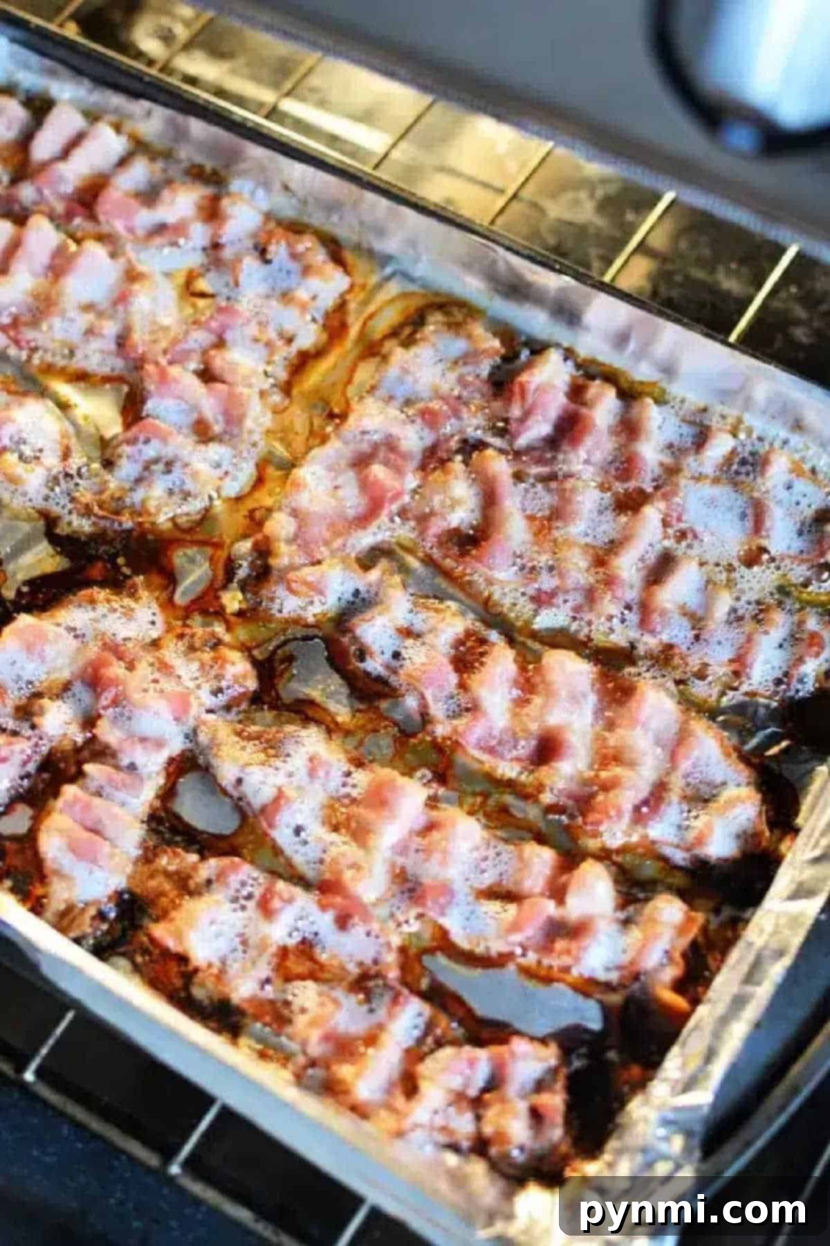 Bacon strips sizzling on a foil-lined baking sheet inside an oven show exactly how to cook bacon in the oven with aluminum foil, ensuring even cooking and minimal mess.