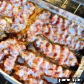 Bacon strips sizzling on a foil-lined baking sheet inside an oven show exactly how to cook bacon in the oven with aluminum foil.