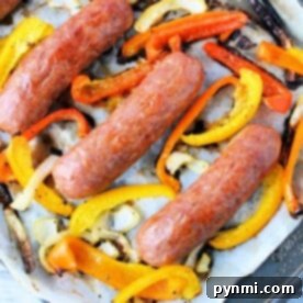 Four Italian sausages on a baking sheet with sliced yellow, orange, and red bell peppers and onions—perfect for making Italian Sausage in Oven 400 for a flavorful and easy dinner.