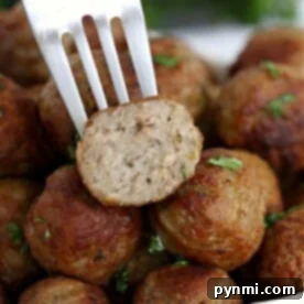 A fork holds a halved meatball over a pile of oven-cooked meatballs, perfectly garnished with herbs.