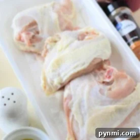 Raw chicken pieces, perfect for bone in chicken breast recipes, rest in a white tray near bottles of spices, olive oil, and fresh parsley on a light-colored surface.