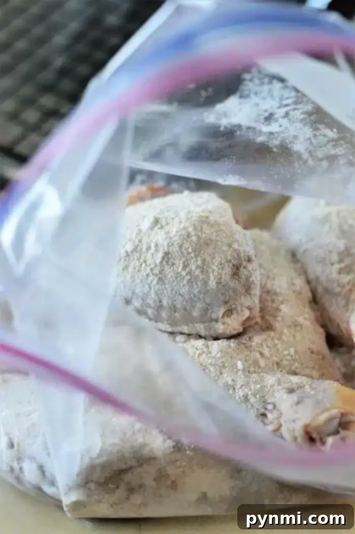 Oven-Baked Chicken Drumsticks 4 An open plastic bag containing raw, floured chicken pieces rests on a kitchen counter. The chicken pieces are coated with flour, ready for further preparation like turning them into delicious baked chicken legs. The background shows a partial view of a dark kitchen appliance.