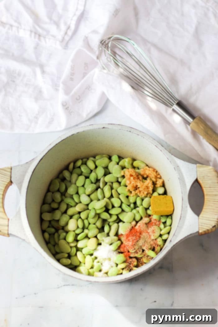 A hand stirring a pot of dry lima beans cooking on the stovetop with various seasonings, demonstrating the cooking process.