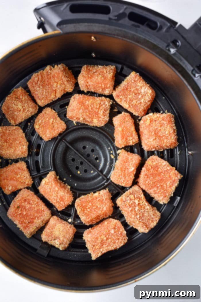 Breaded salmon pieces, similar to delectable salmon bites, sit in an air fryer basket, ready to be cooked.