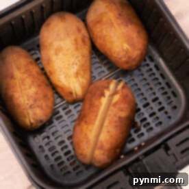 Four whole potatoes, with slits on top, are ready to reheat as they sit neatly in the air fryer basket.