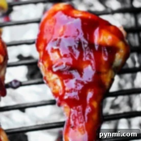Smoked chicken drumsticks and grilled wings are basted in rich barbecue sauce, sizzling together on a grill with aluminum foil catching every delicious drip.