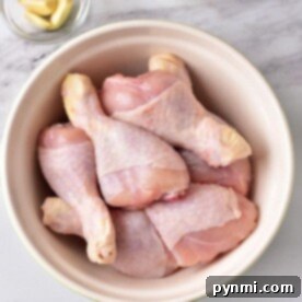 Delicious Chicken Leg Dinners 7 Raw chicken drumsticks in a bowl on a marble surface, accompanied by garlic cloves and a bowl of mayonnaise nearby, ready to inspire the best chicken leg recipes for your next culinary adventure.