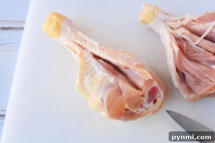 Close-up of a perfectly butterflied chicken leg, generously seasoned with herbs and spices, resting on a white surface, showcasing its readiness for cooking.