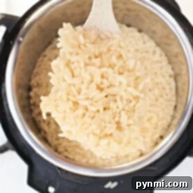 The Secret to Perfectly Cooked Arborio Rice 8 A white spatula lifts perfectly cooked Arborio rice from an electric pressure cooker, demonstrating how to achieve creamy perfection.