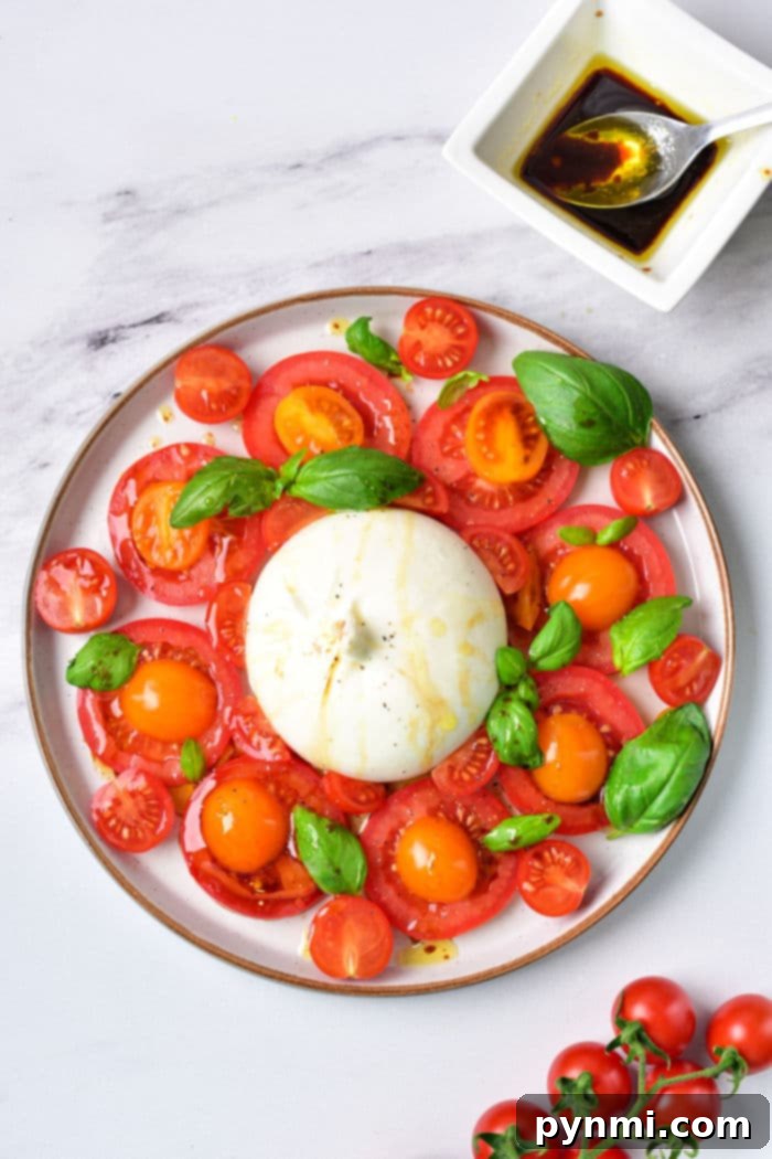 Close-up of a knife slicing into creamy burrata cheese on a Burrata Caprese platter with fresh tomatoes and basil.