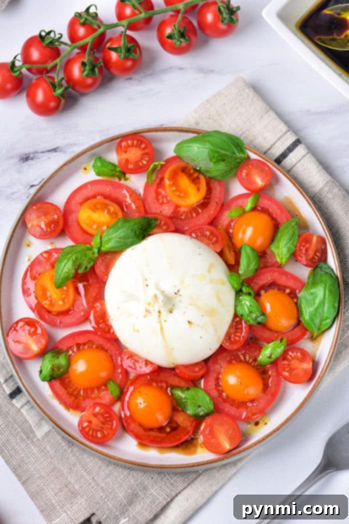 A vibrant Burrata Caprese salad with a whole burrata cheese ball, sliced red tomatoes, and fresh green basil leaves on a white plate, ready to be served.