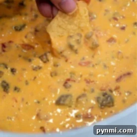 A hand dips a chip into a bowl of creamy Velveeta sausage dip, richly blended with chunks of meat and Rotel tomatoes.