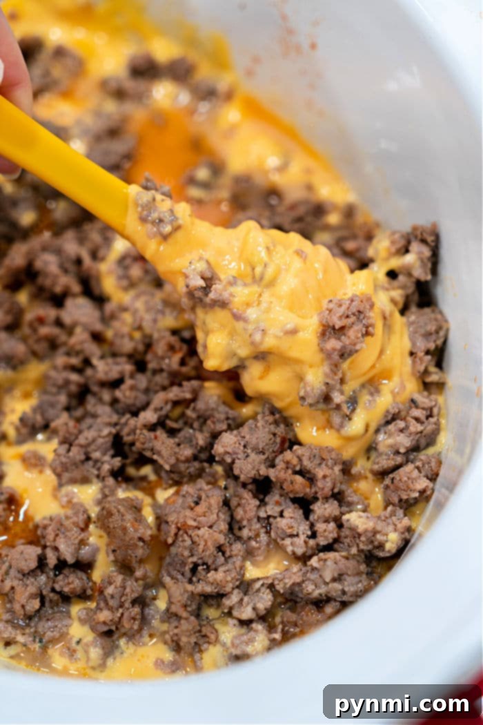 Creamy Velveeta Sausage Rotel Dip 6 Melted Velveeta cheese and browned ground spicy sausage being stirred together in a slow cooker with a yellow spatula, creating a delicious Sausage Dip.