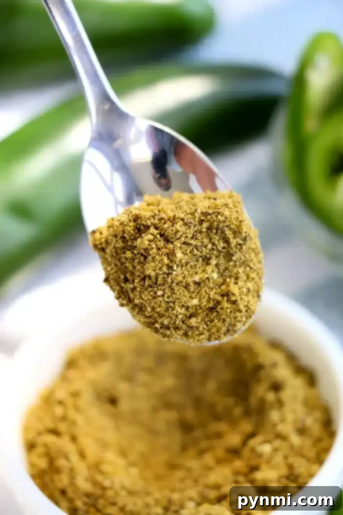 A close-up image of a spoonful of vibrant green jalapeno powder held above a white bowl filled with the same fiery seasoning. In the background, blurred green peppers are visible, hinting at the spice's origin and adding depth to this flavorful scene.
