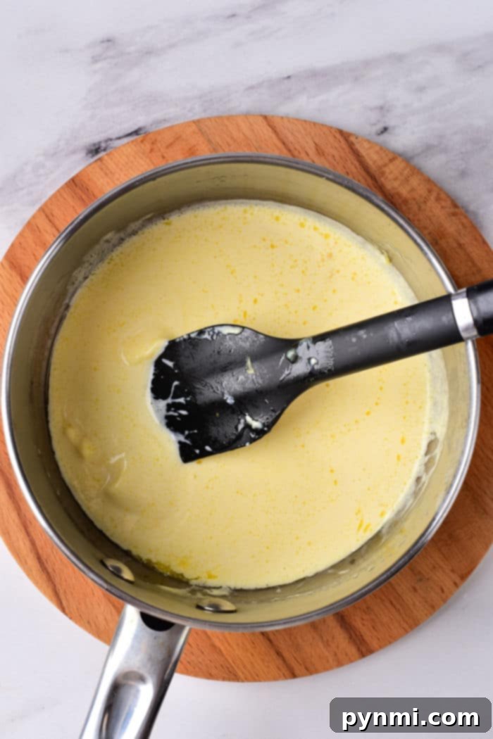 A black spatula gracefully stirs creamy rich Cajun Alfredo sauce, all set on a rustic wooden board.