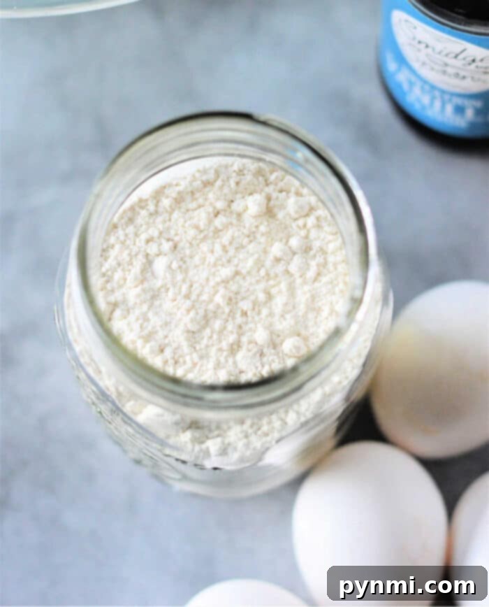 Cracker Barrel-Inspired Homemade Pancake Mix 2 A jar filled with homemade pancake mix sits elegantly on a wooden surface, surrounded by fresh eggs and a bottle, suggesting the ingredients are ready for a delicious breakfast. This setup highlights the ease of preparing Cracker Barrel style pancakes from scratch.